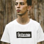 Casual portrait of a young man wearing a white t-shirt with future print, wooden background.